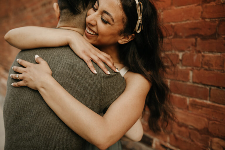 Engaged couple in Toronto hug and smile as their engagement photographer takes their picture.